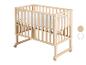 Lit bébé en bois clair avec literie blanche et roulettes.