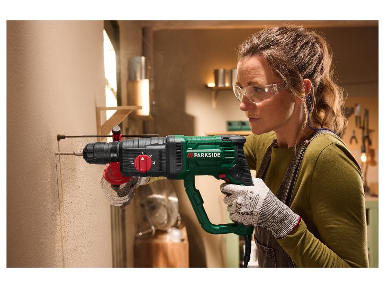 Femme avec lunettes de sécurité et gants perçant un mur avec une perceuse PARKSIDE.