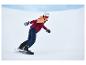 Femme en snowboard avec un casque blanc, une veste orange et bordeaux, et un pantalon bleu foncé.