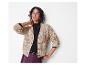 Lachende vrouw in een beige gebreide cardigan en bordeauxrode leren broek.