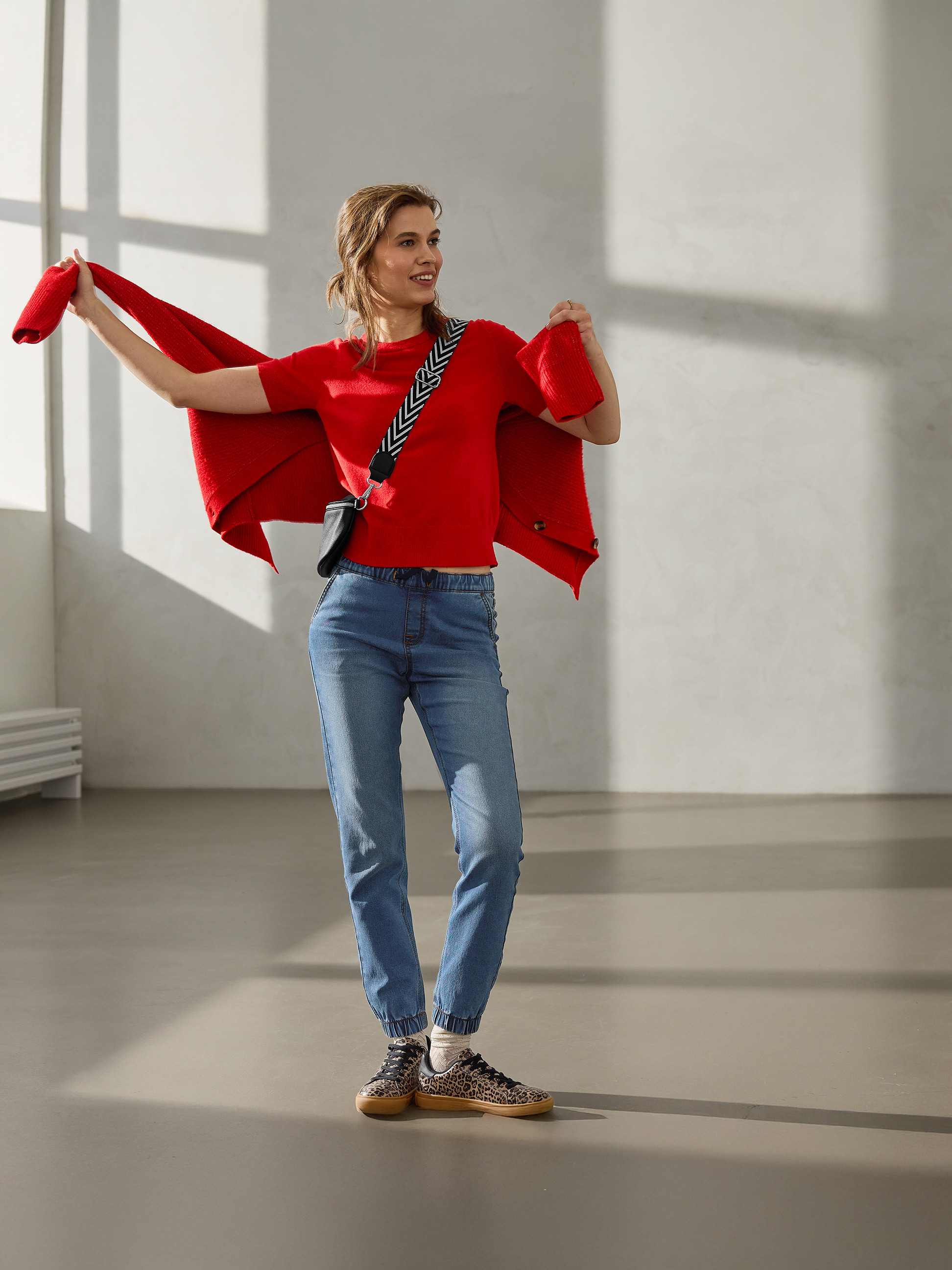 Femme en pull rouge, cardigan rouge, jean et baskets à imprimé léopard.