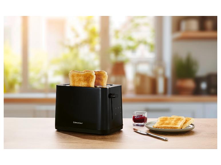 Zwarte broodrooster met twee sneetjes toast, jam en een mes op een houten tafel.