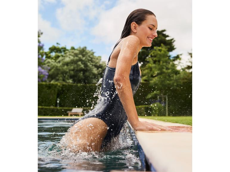 Vrouw in een donkere badpak uit een zwembad komt.