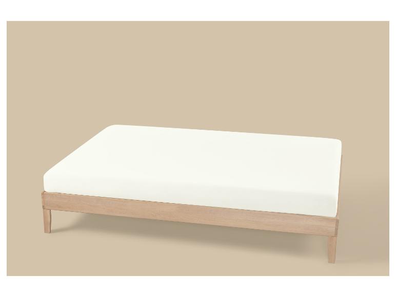 Sommier en bois clair avec matelas blanc sur fond beige.