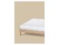 Wit matras op een licht houten bedframe tegen een beige achtergrond.