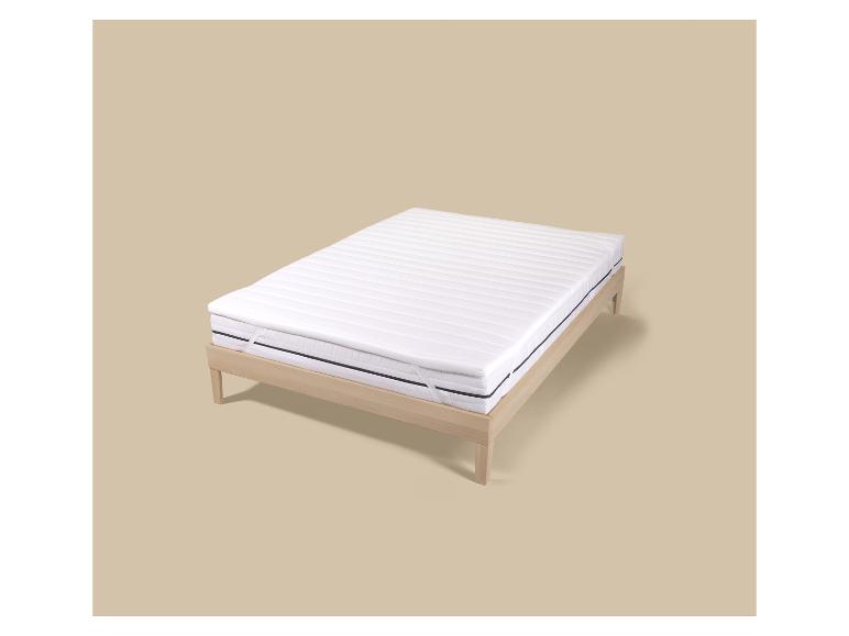 Wit matras met topper op een licht houten bedframe.