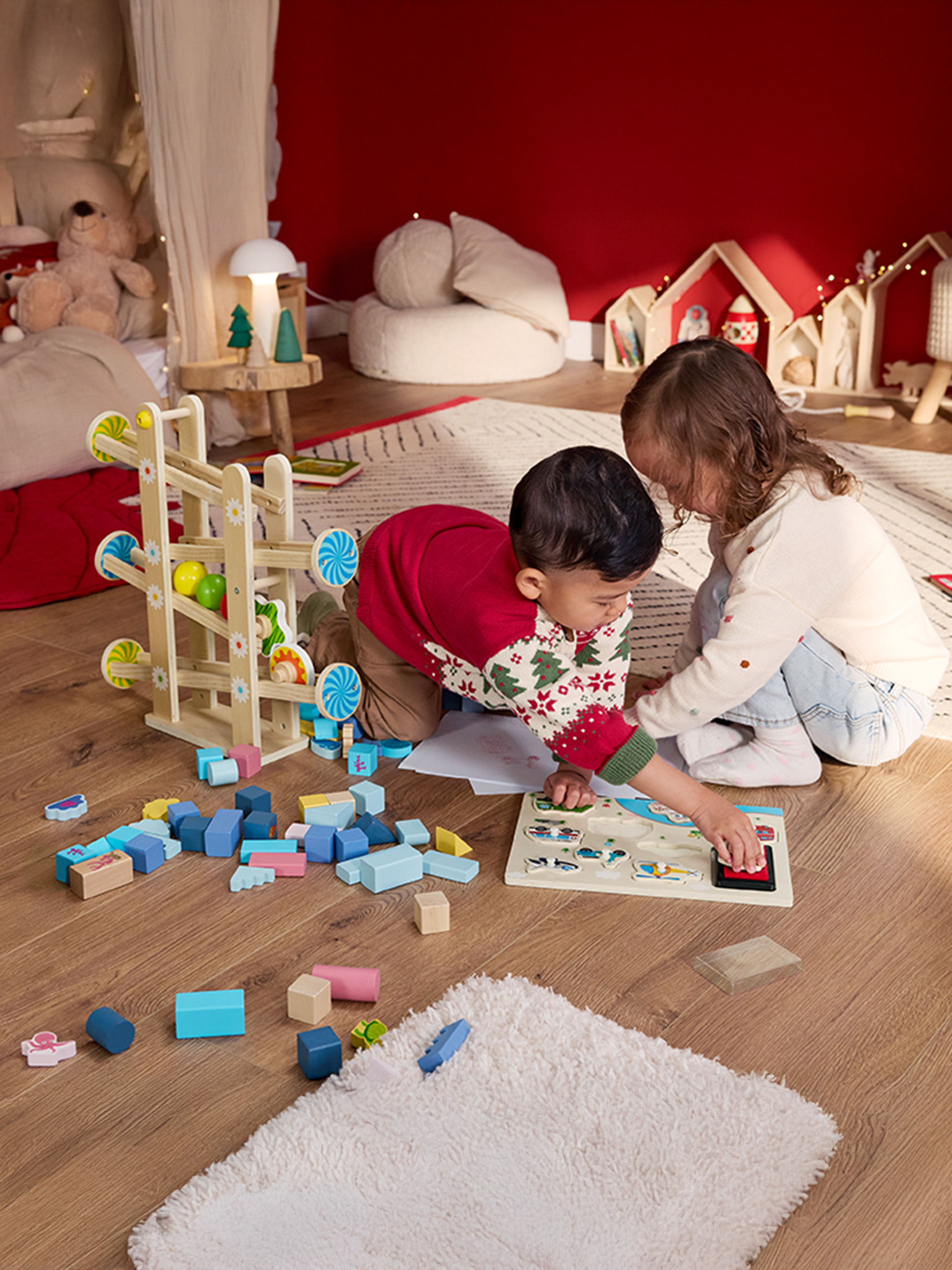 Twee kinderen spelen met houten speelgoed en een knikkerbaan op een houten vloer.