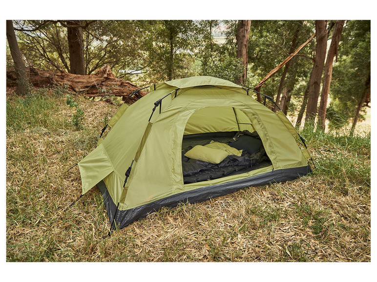 Une tente verte avec un sac de couchage et un oreiller dans une forêt.