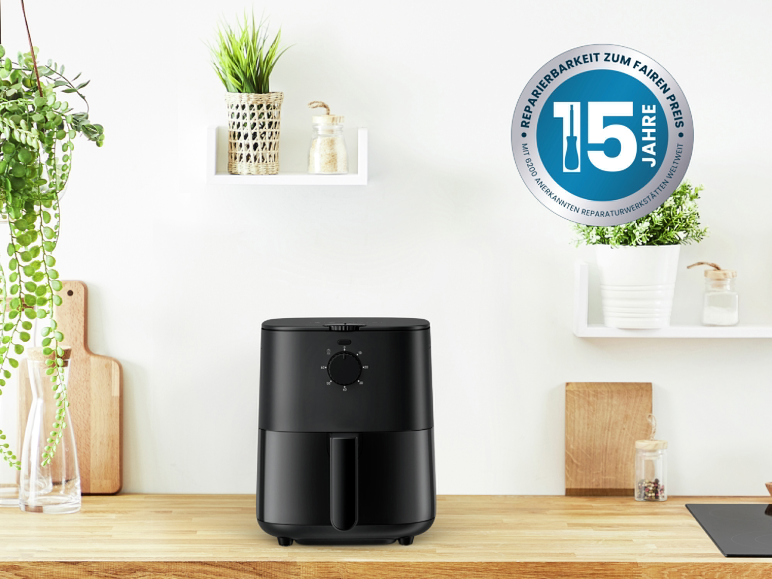 Zwarte airfryer op een houten aanrecht met planten en planken.