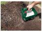 Man strooit witte korrels met een Parkside handstrooier in de tuin.