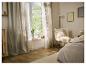 Lichte slaapkamer met beige gordijnen, houten vloer en witte fauteuil met kussen.