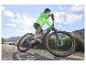 Un homme en veste vert néon conduit un vélo électrique Maxxis sur un chemin de terre.
