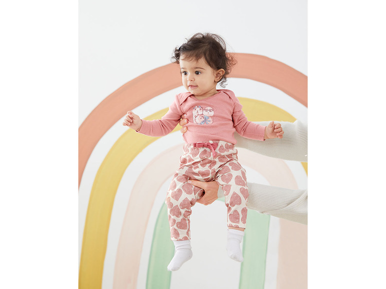 Een baby in roze kleding met hartjesprint.