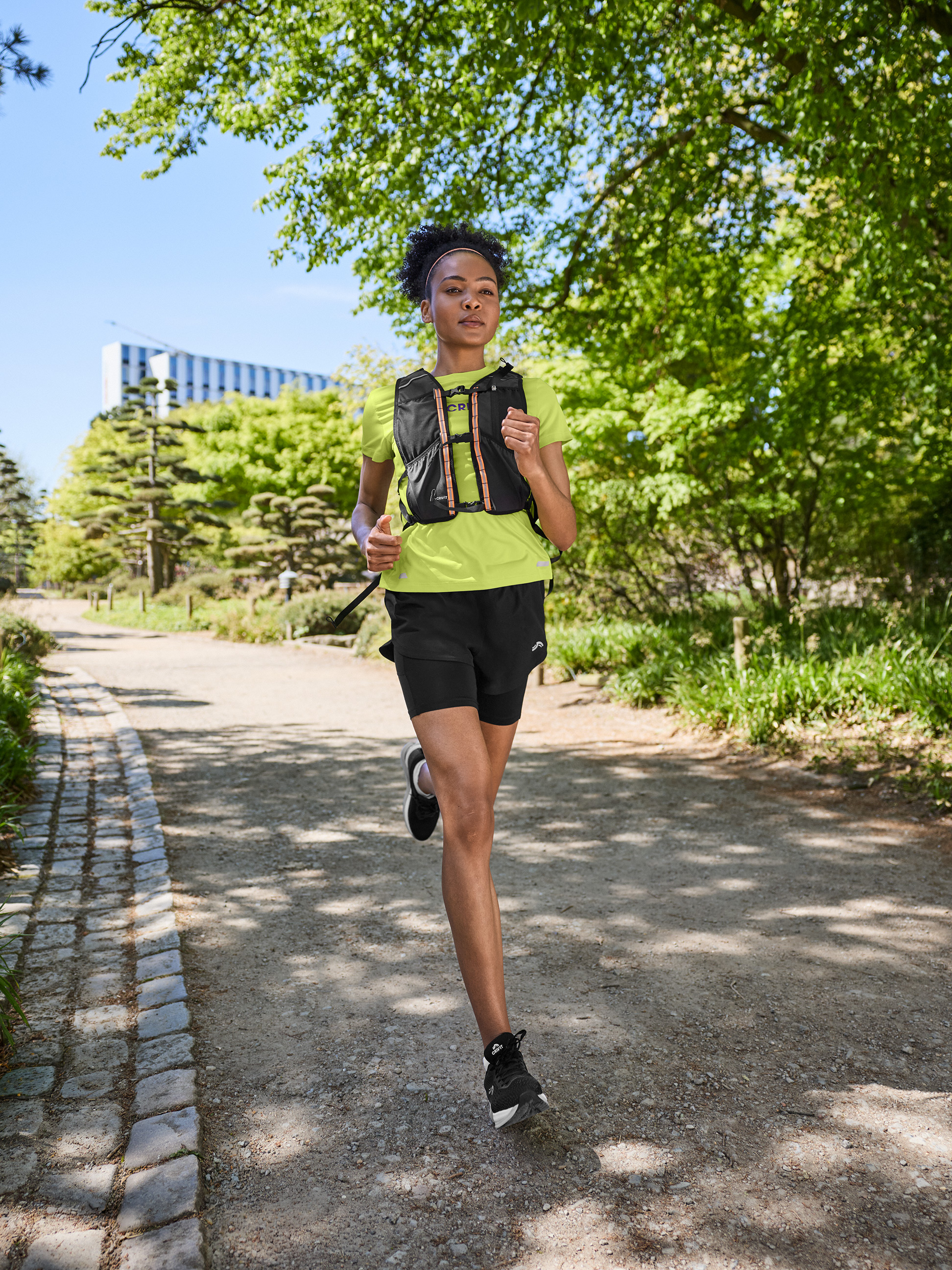 Vrouw in sport-T-shirt, korte broek en hardloopvest, joggend op een zandpad.