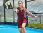 Femme en robe de sport bordeaux jouant au padel avec une raquette noire et une balle jaune.