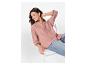 Femme souriante en chemise rose et jean assise sur une chaise blanche.