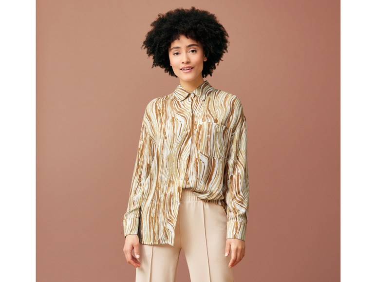 Une femme porte un pantalon beige et une chemise à motif abstrait.