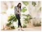Femme en veste grise et leggings noirs avec baskets blanches devant des plantes.
