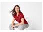 Vrouw in een rood poloshirt en grijze jeans zittend op een witte stoel.