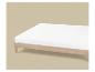Lit en bois avec matelas blanc sur fond beige.