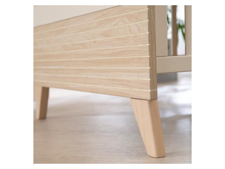 Pieds et panneau latéral en bois clair d'un lit bébé.