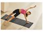 Femme en débardeur rose et short noir faisant du yoga sur un tapis gris.