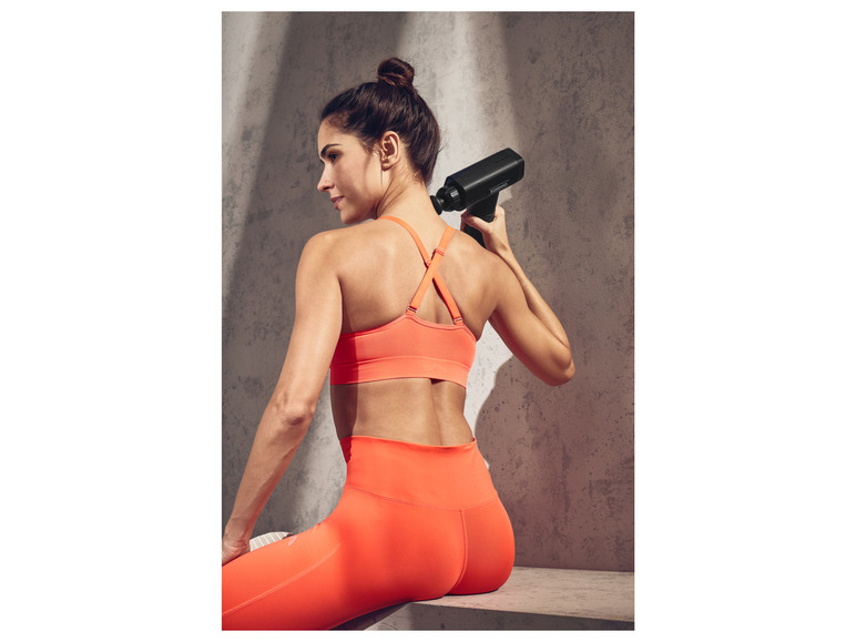 Een vrouw in sportkleding gebruikt een massagepistool van het merk Hyperice.