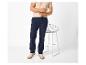 Homme en t-shirt beige et pantalon bleu marine, debout à côté d'une chaise.