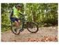 Man in neongele jas en blauwe korte broek fietst op een e-bike op een bospad.