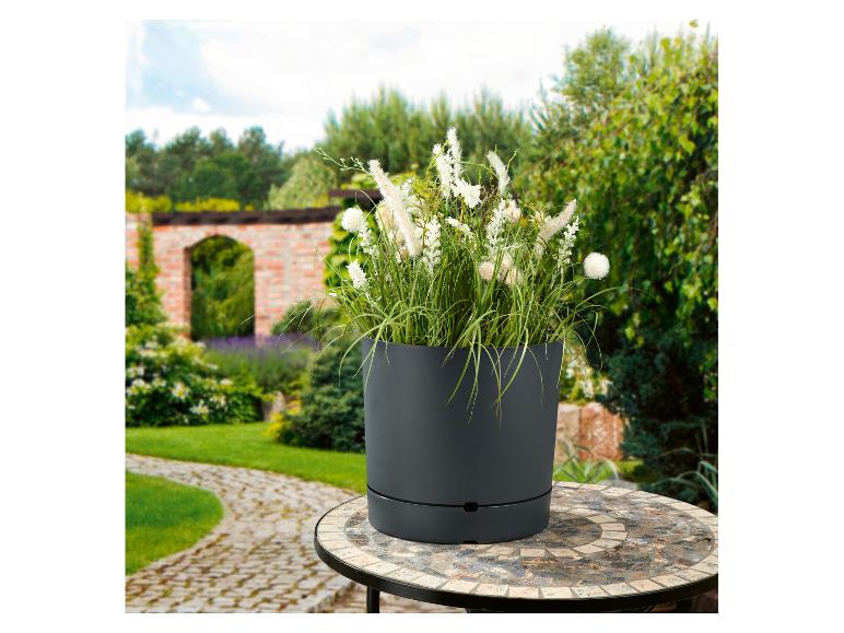 Pot de jardin gris avec des fleurs blanches sur une table en mosaïque dans un jardin.
