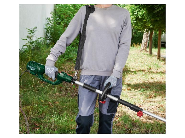 Persoon gebruikt elektrische heggenschaar met draagriem in een tuin.