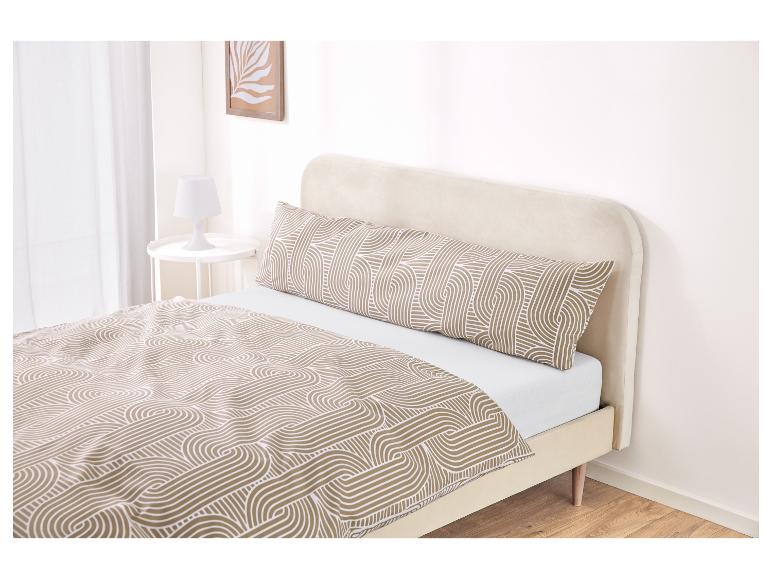 Een bed met een beige hoofdbord en een dekbed en lichaamskussen met patroon.