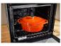 Oven met oranje gietijzeren pan op een rooster.
