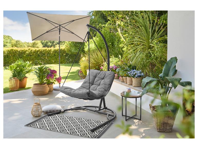 Grijze hangstoel met kussen, parasol en planten op een terras.