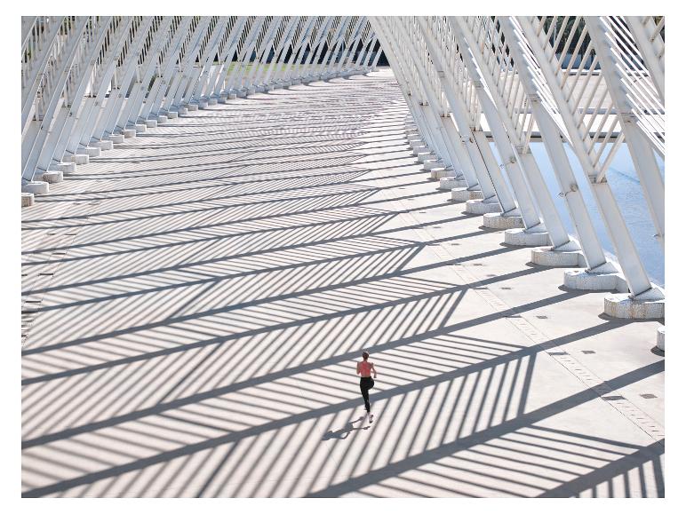 Vrouw rent over brug met witte metalen constructies en lange schaduwen