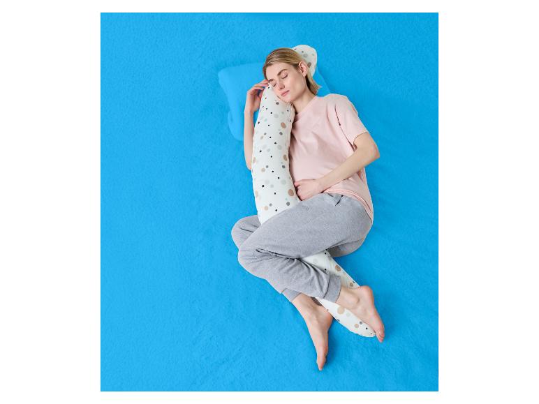 Vrouw slaapt op haar zij met een lichaamskussen op een blauw laken.