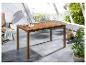 Houten tuineettafel met lattenblad, op een terras met stoel en planten.