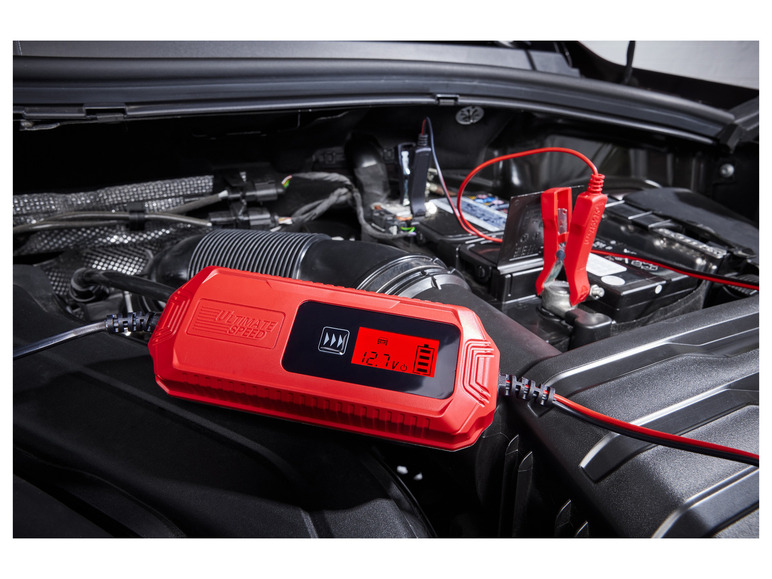 Un chargeur de batterie Ultimate Speed ​​rouge avec des pinces connectées à une batterie de voiture.