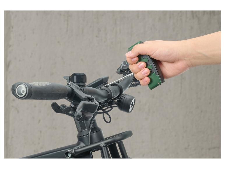 Main tenant un outil vert sur le guidon d'un vélo avec accessoires.