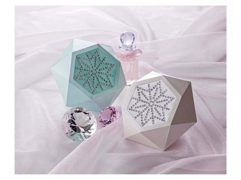 Deux boîtes avec des flocons de neige et un flacon de parfum sur un tissu rose.
