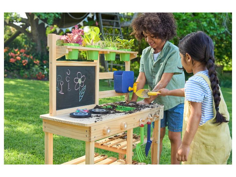 Deux enfants jouent avec une cuisine en bois pour enfants avec un bac à sable et des pots de fleurs.