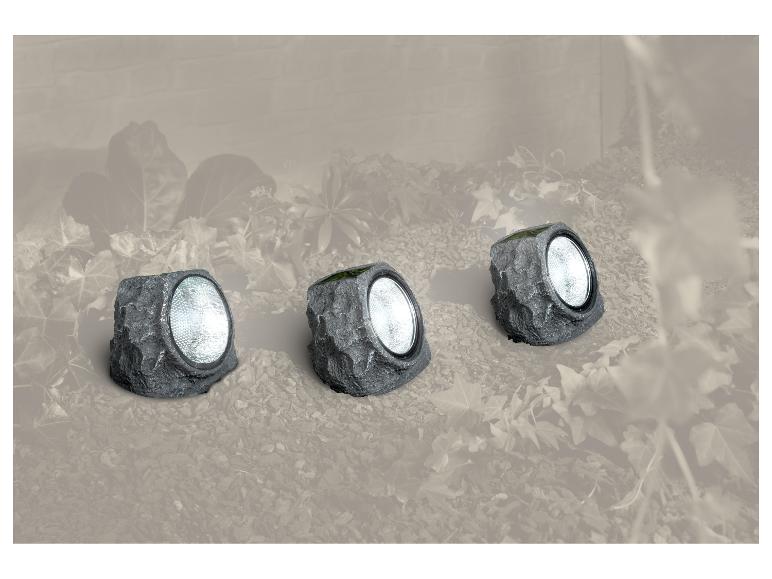 Drie grijze rotsvormige tuinlampen op zonne-energie, geïntegreerd in een tuinomgeving.