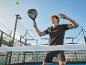 Man speelt padel met racket, bal en baan op de achtergrond.