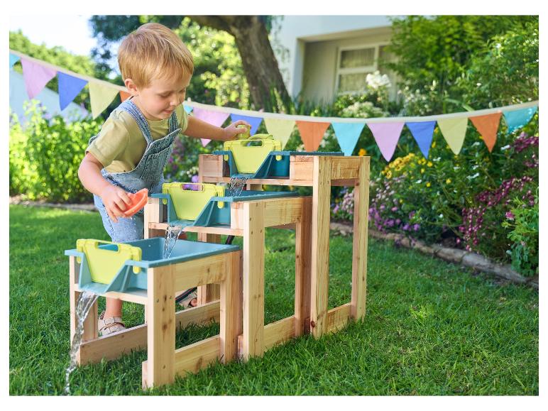 Een kind speelt met een houten waterbaan met groene bakken in de tuin.