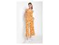 Vrouw in een oranje jumpsuit met witte bladprint en witte sneakers.
