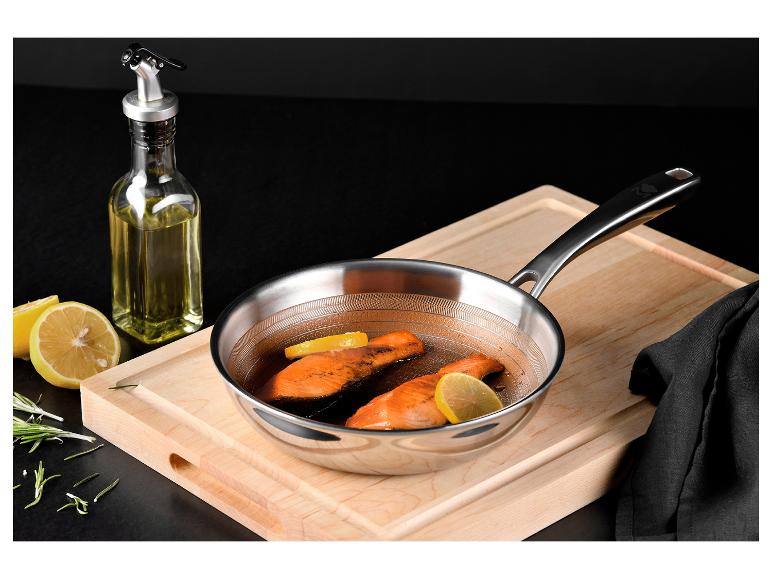 Poêle en acier inoxydable avec deux morceaux de saumon, du citron et une bouteille d'huile d'olive.