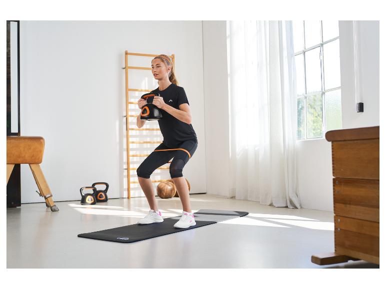 Vrouw doet squats met een kettlebell, met een weerstandsband om haar dijen.