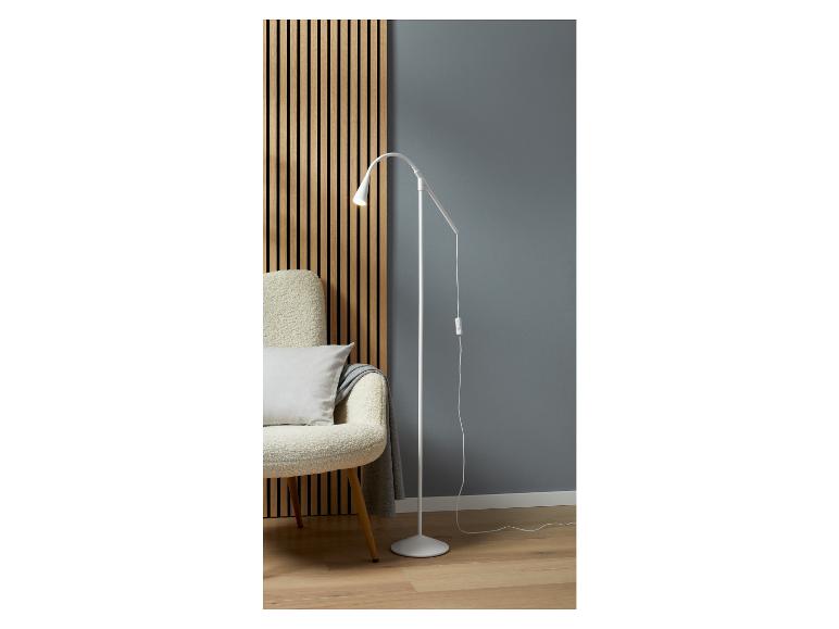 Een witte staande lamp met een gebogen arm, naast een fauteuil met een plaid.