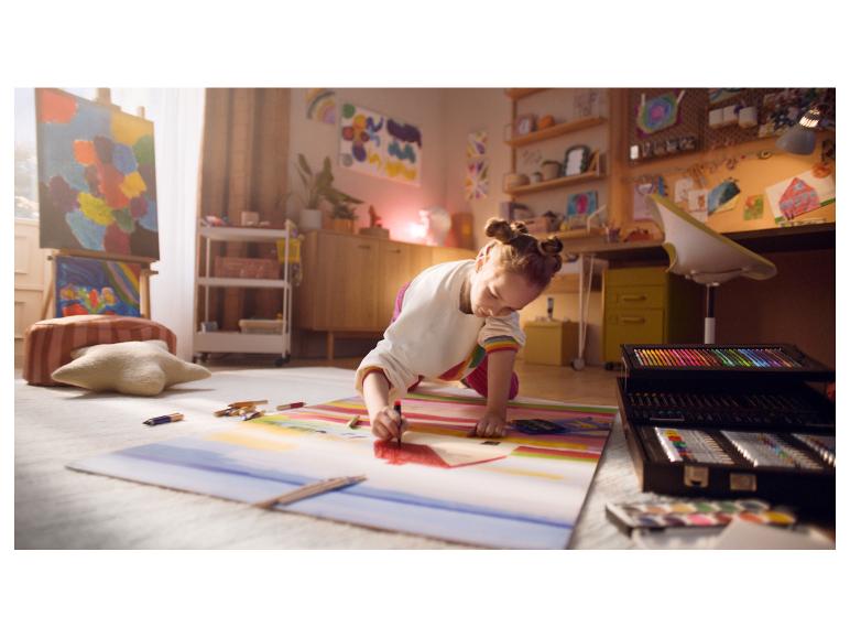 Une fille dessine par terre avec un grand set d'art dans une pièce pleine d'art.