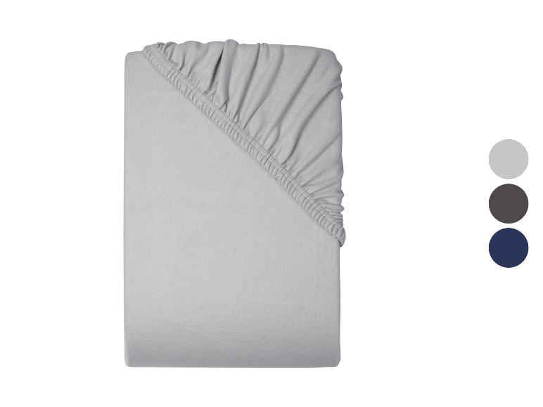 Un drap-housse gris clair, plié, avec trois échantillons de couleurs à droite : gris clair, gris foncé et bleu marine.